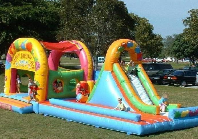 Colorful inflatable slide and bounce house set up on grass at a park, with children playing nearby