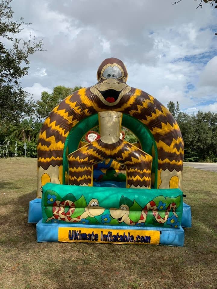 Inflatable monkey-themed bounce house with colorful arches and blue base outdoors under cloudy sky