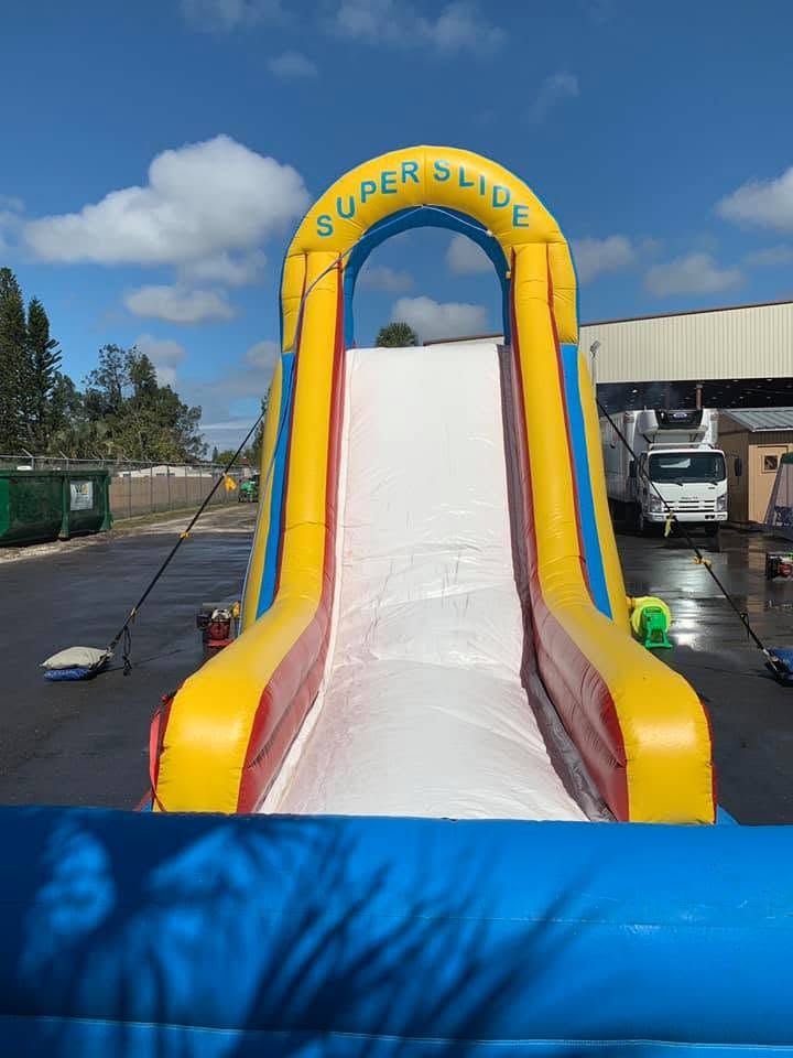 Inflatable yellow-and-blue super slide with a white sliding lane outdoors in a fairground lot