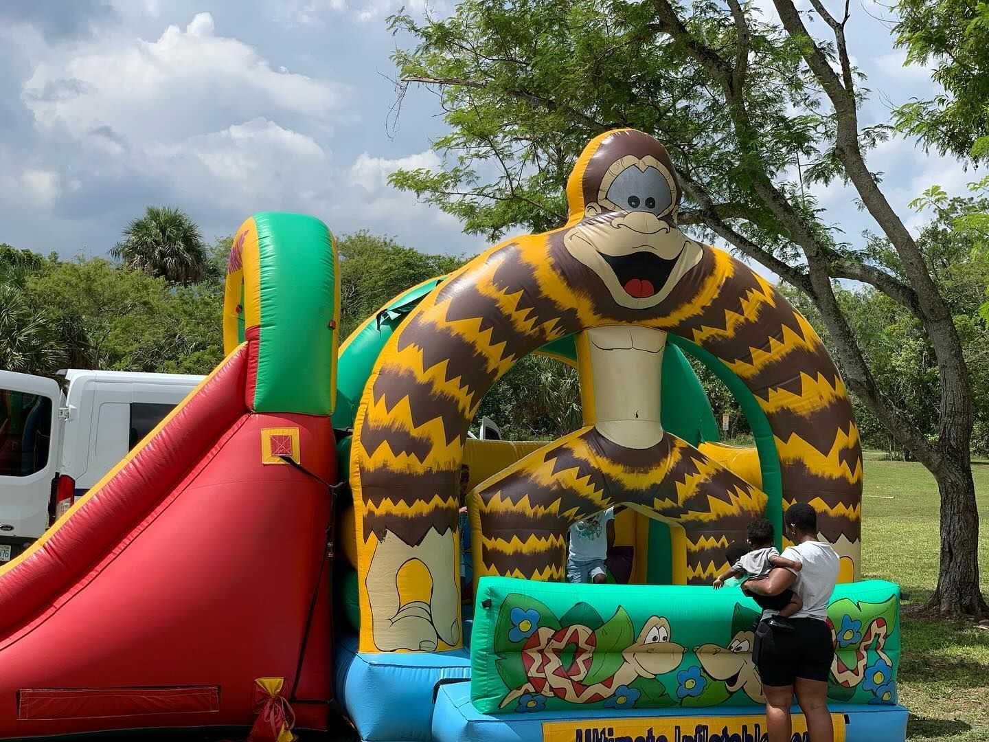 Colorful inflatable tiger-and-arch playground with a red slide outdoors; child playing in front.