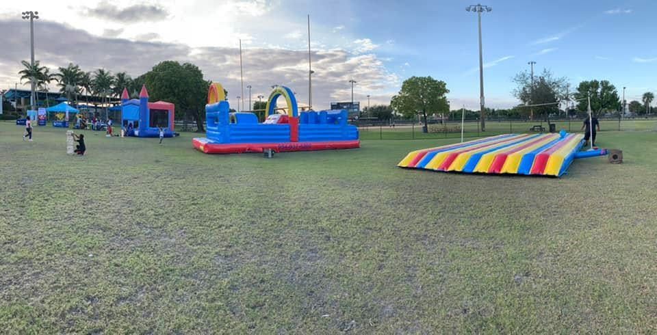 Colorful inflatable playground on a grassy field under cloudy skies, with children playing nearby.