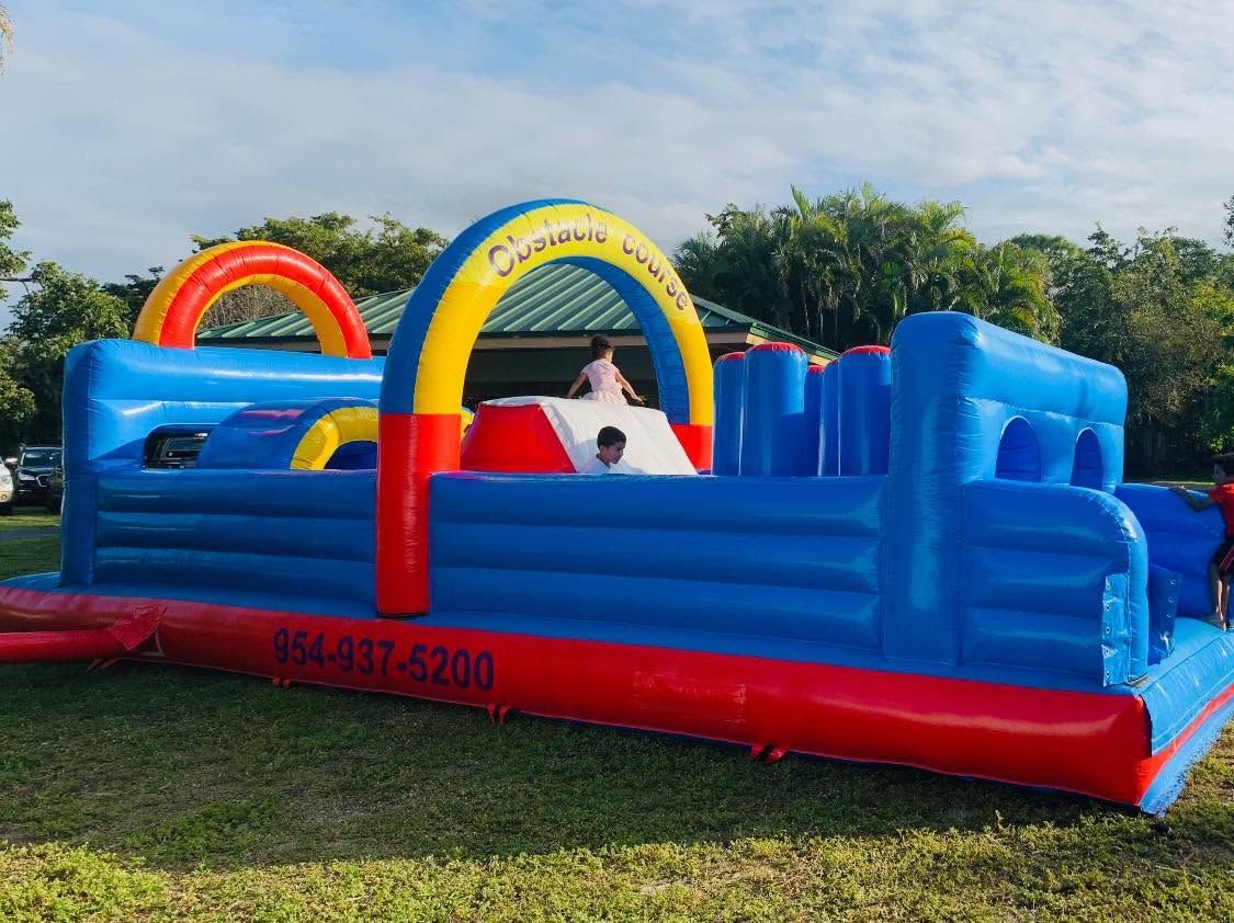 Blue and red inflatable bounce house with rainbow arches on a grassy field outdoors