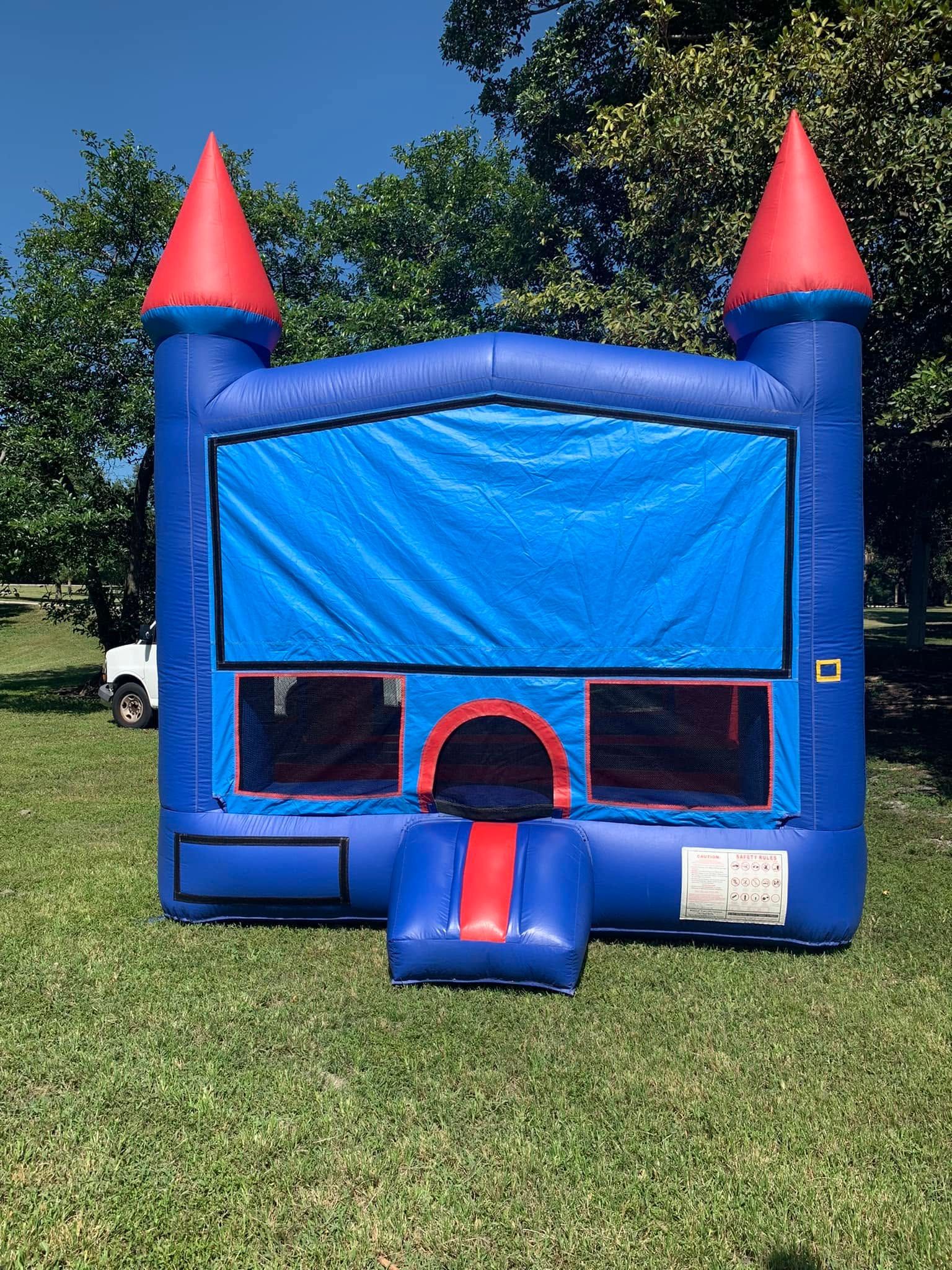 Blue inflatable bounce house with red roof cones and front slide on a grassy field.