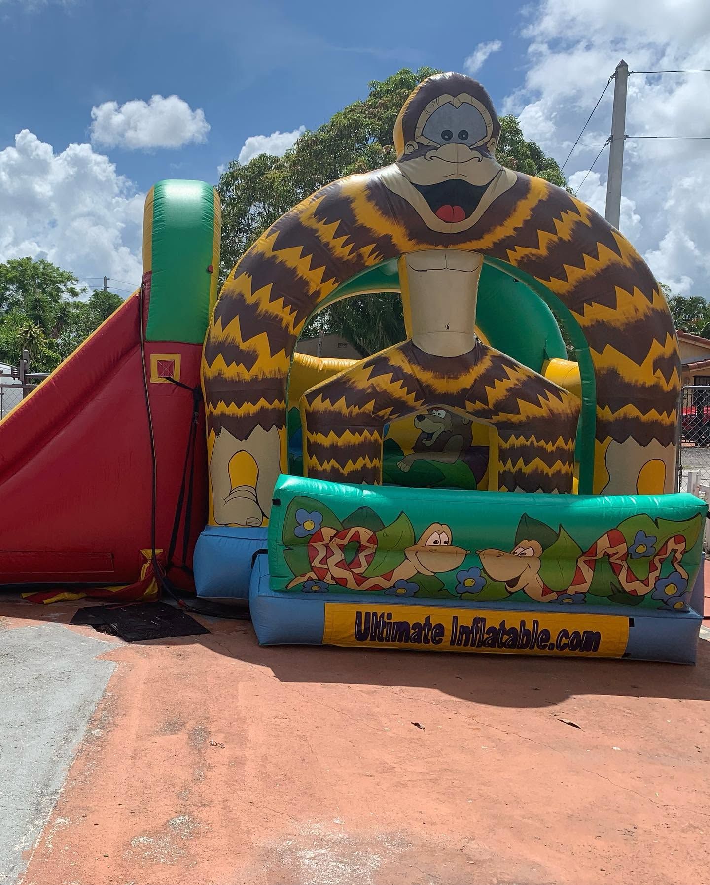 Colorful inflatable monkey slide with jungle pattern at an outdoor park under a cloudy sky