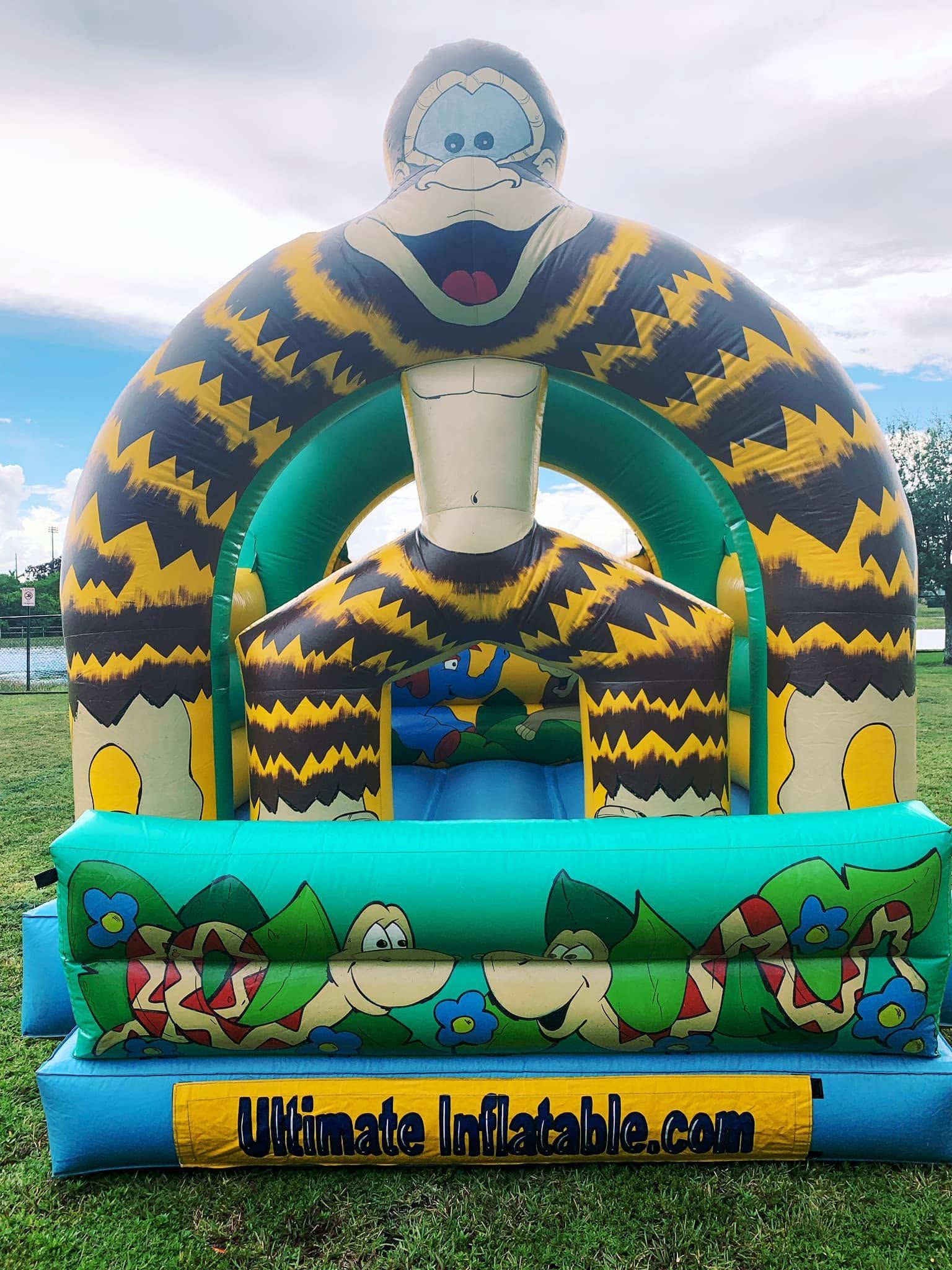 Blue and yellow inflatable bounce house with cartoon dinosaurs on the front, outdoors under a cloudy sky