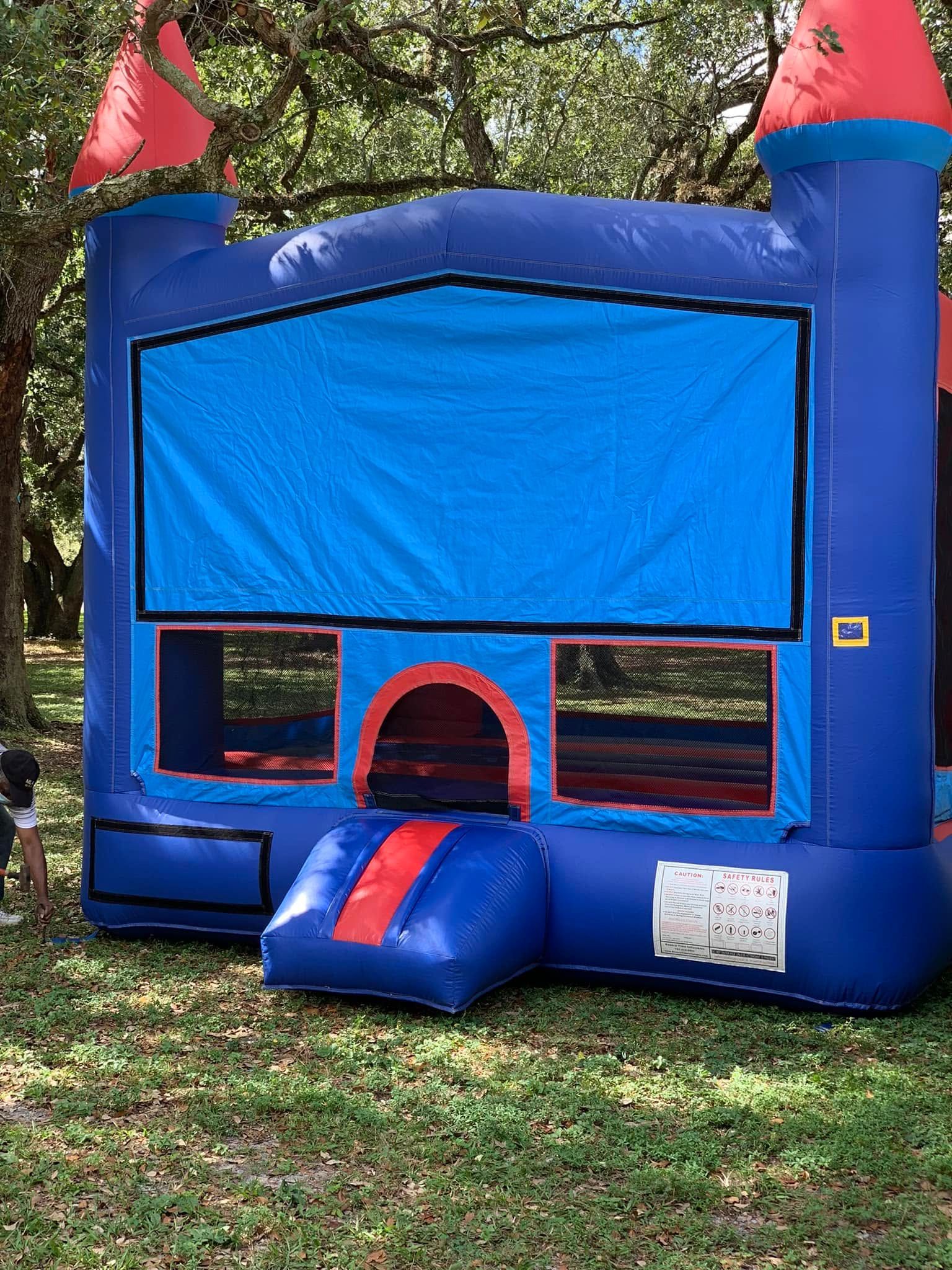 Blue inflatable bounce house with red corner towers and a front entrance on grass outdoors