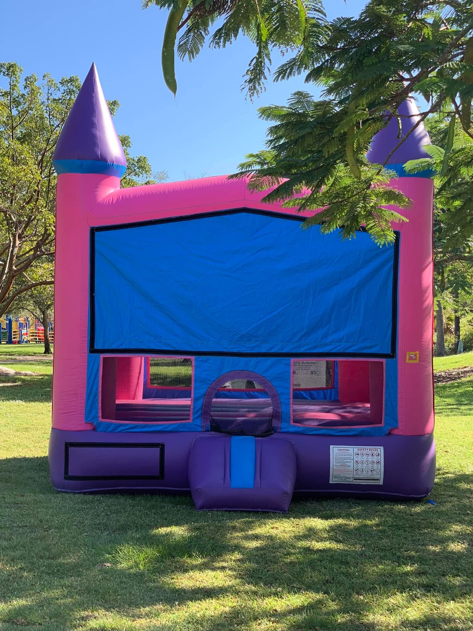 Pink-and-purple inflatable bounce house with blue front panel in a sunny grassy park