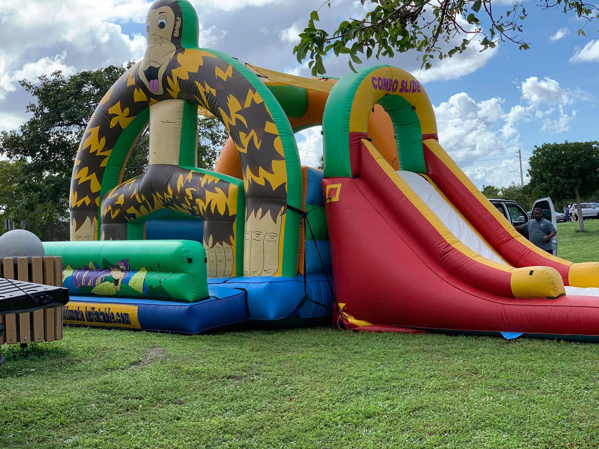 Colorful inflatable bounce house with red slide and green arches on a grassy field under a cloudy sky