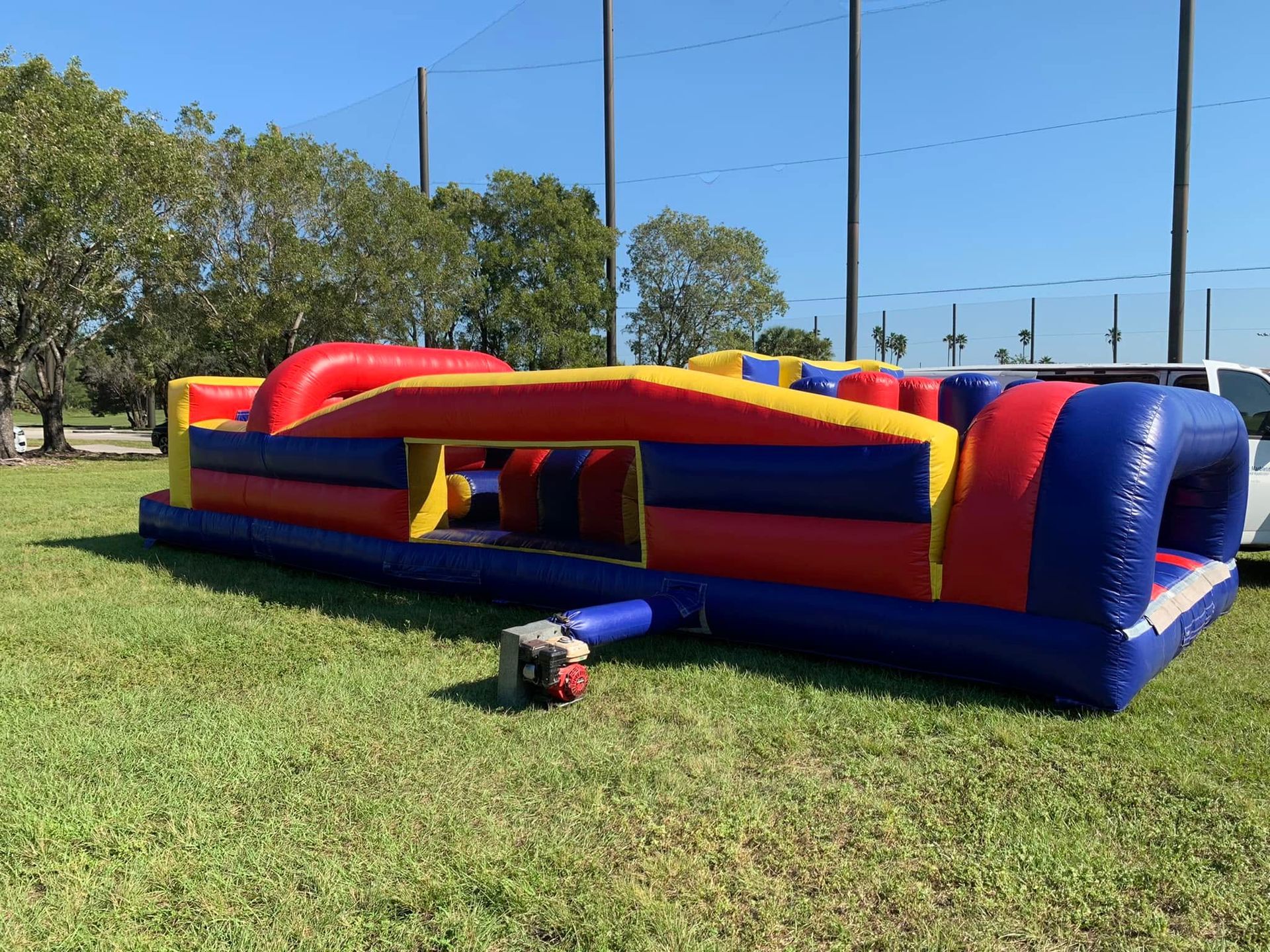 Colorful inflatable obstacle course on a grassy field near a baseball fence and trees.