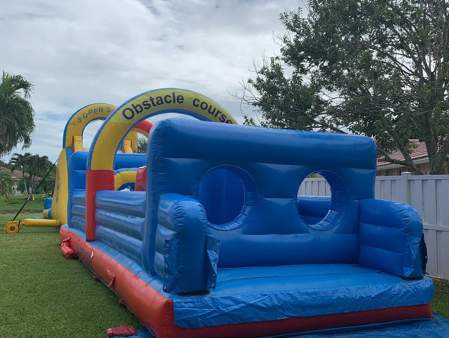 Blue inflatable obstacle course on grass with yellow arches and trees in the background
