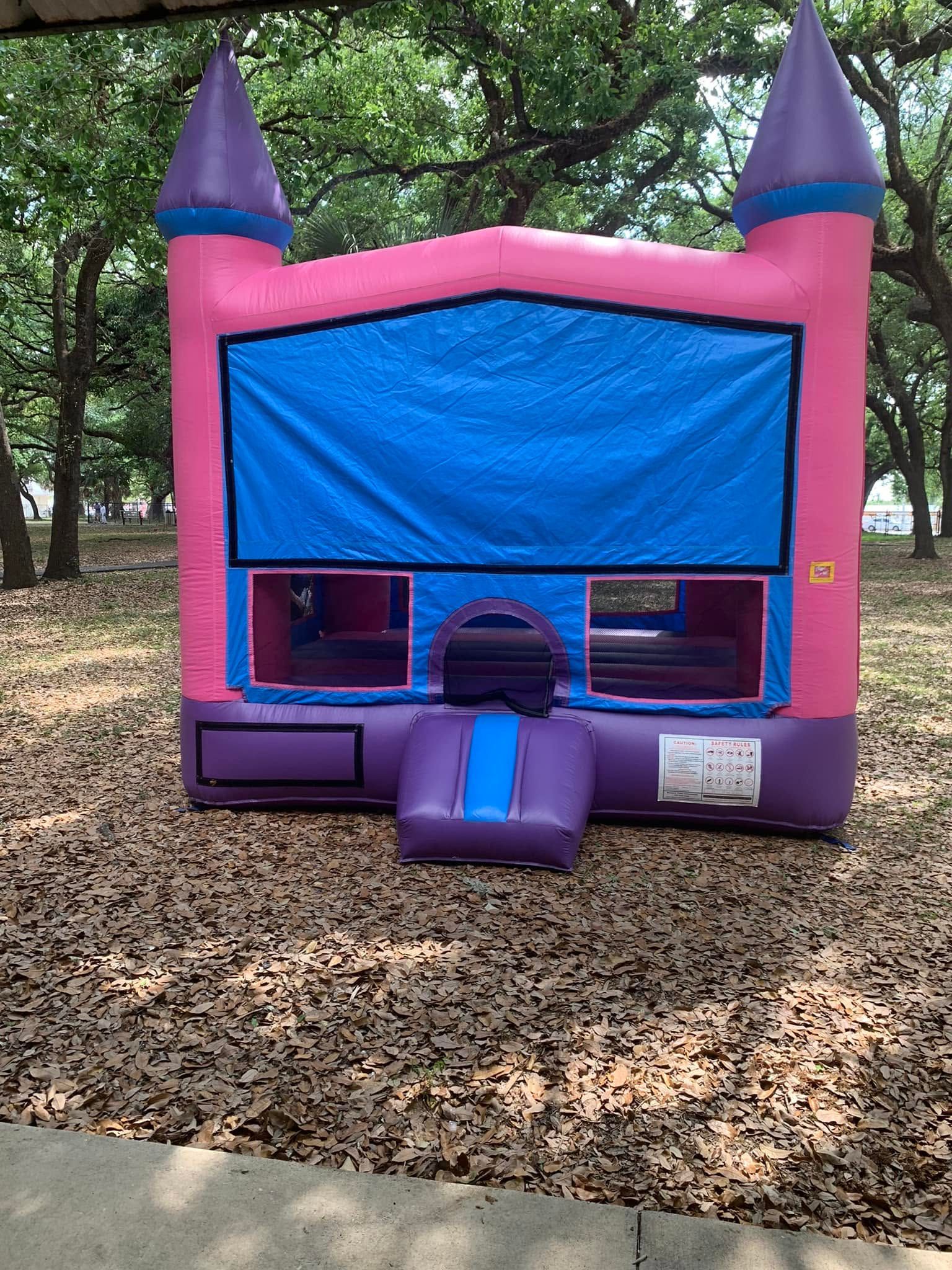 Pink and purple inflatable bounce house with blue front panel in a wooded outdoor area