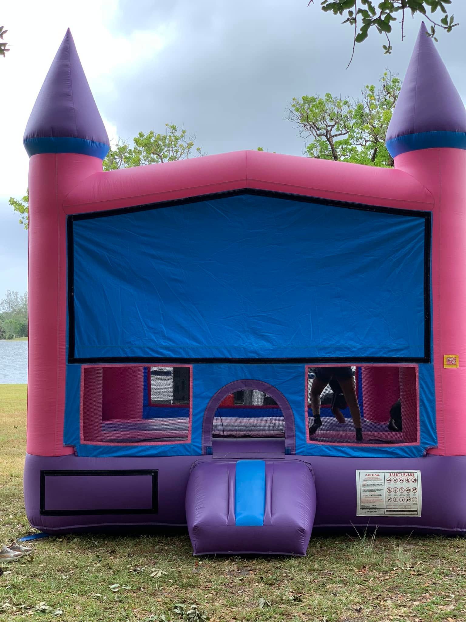 Purple and pink bounce house with blue windows and twin turrets outdoors
