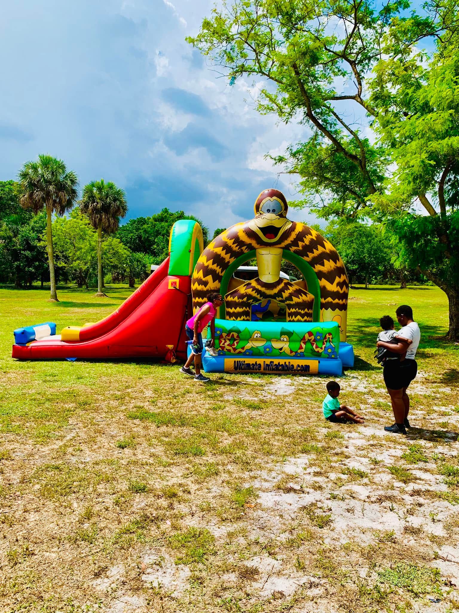Colorful inflatable slide and play structure in a grassy park with a few people nearby