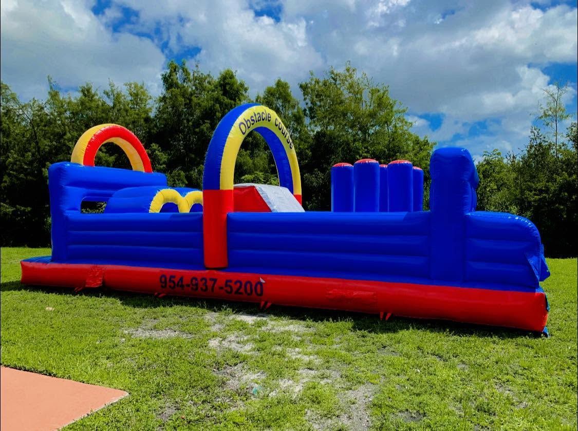 Blue inflatable obstacle course on grass with red base and yellow arches under a cloudy sky