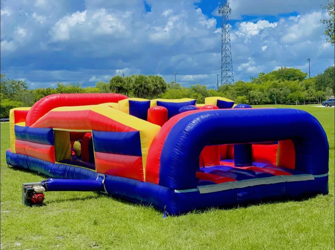 Red, blue, and yellow inflatable obstacle course on a grassy field under a cloudy sky