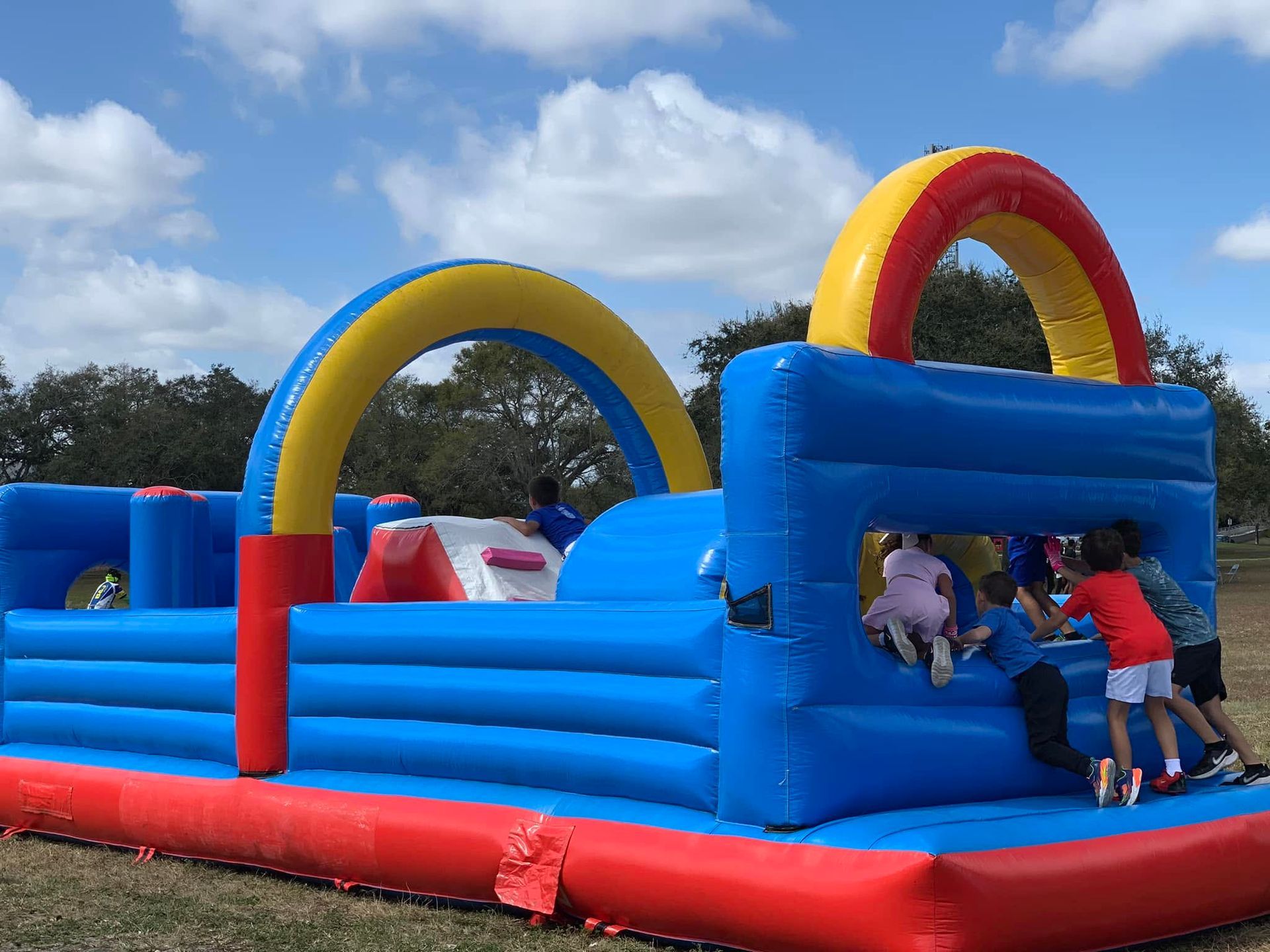 Children climbing on a blue and red inflatable bounce house with yellow and red arches outdoors
