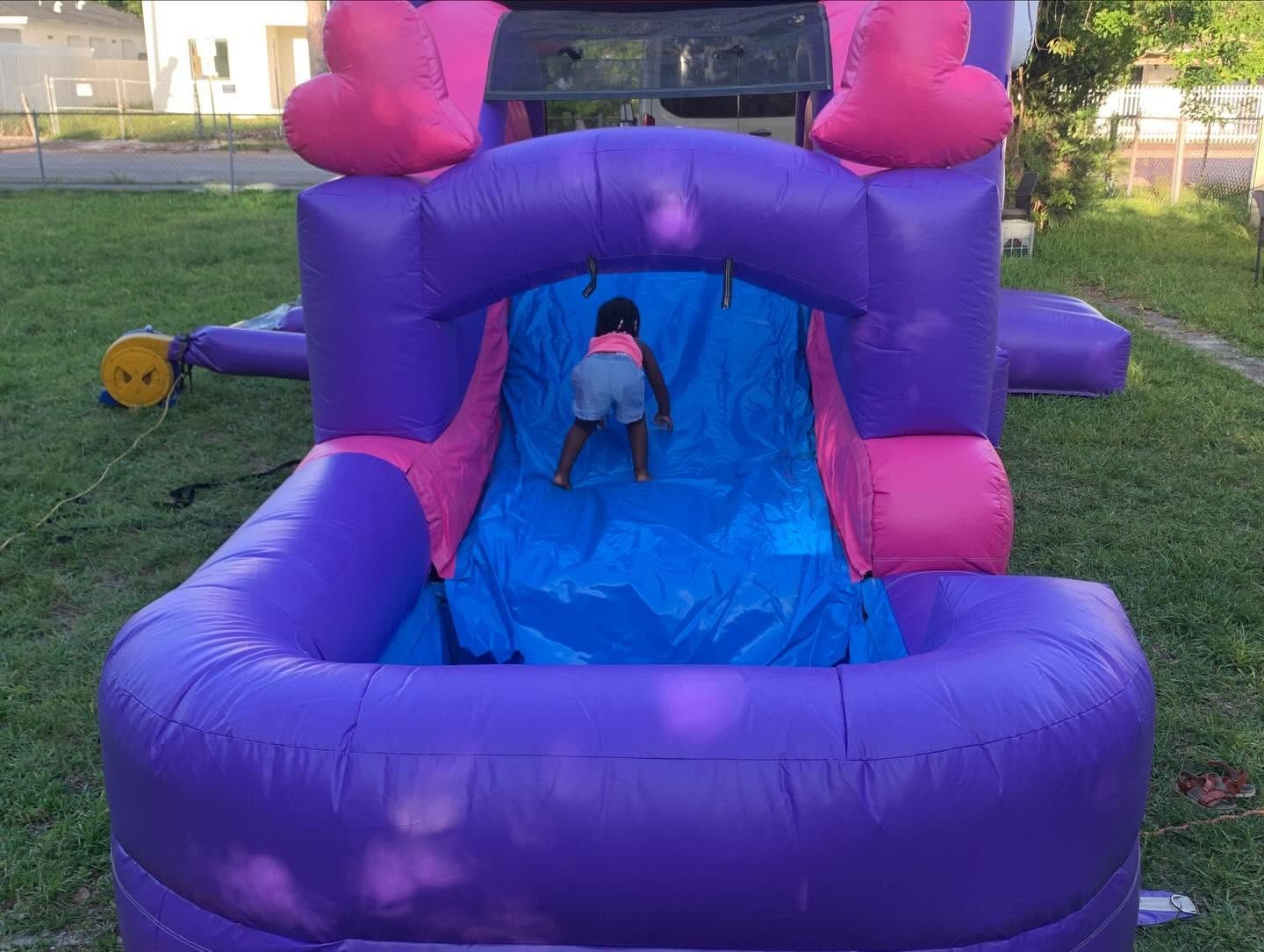 Child climbing a purple and pink inflatable slide in a grassy yard