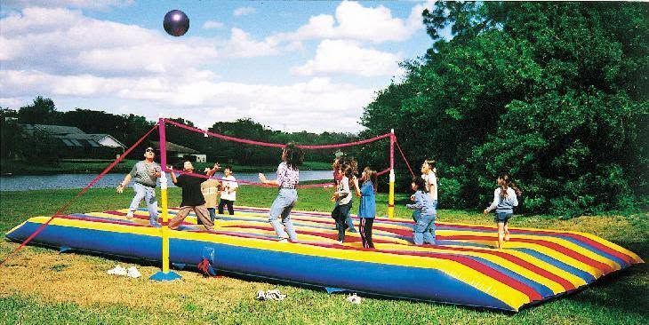 Children bouncing on a colorful inflatable jump pad outdoors, with a ball in the air.