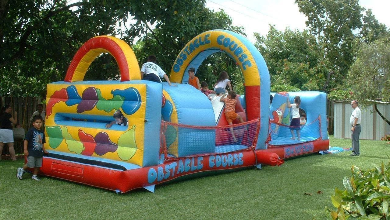 Colorful inflatable bounce house with children playing in a grassy park, trees in the background.