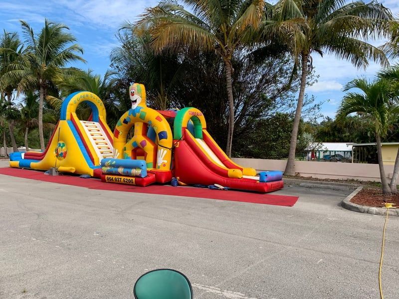 Colorful inflatable bounce house with slide in a palm-lined parking lot on a sunny day
