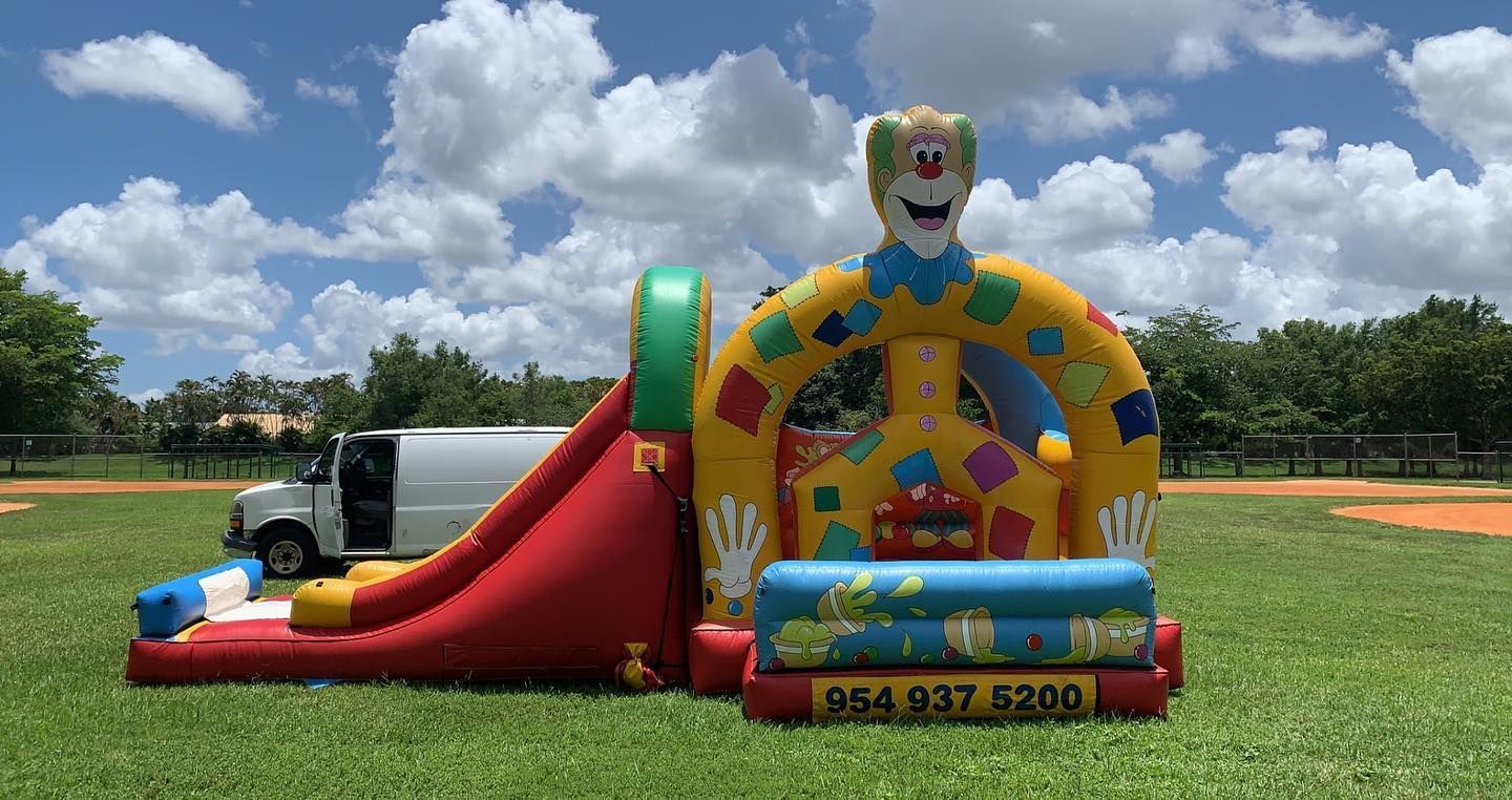 Colorful inflatable clown bounce house and slide on a grassy field under a cloudy sky