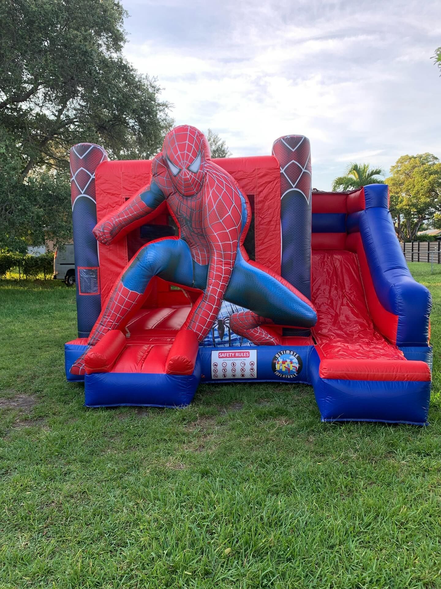 Spider-Man bounce house with slide on a grassy lawn outdoors