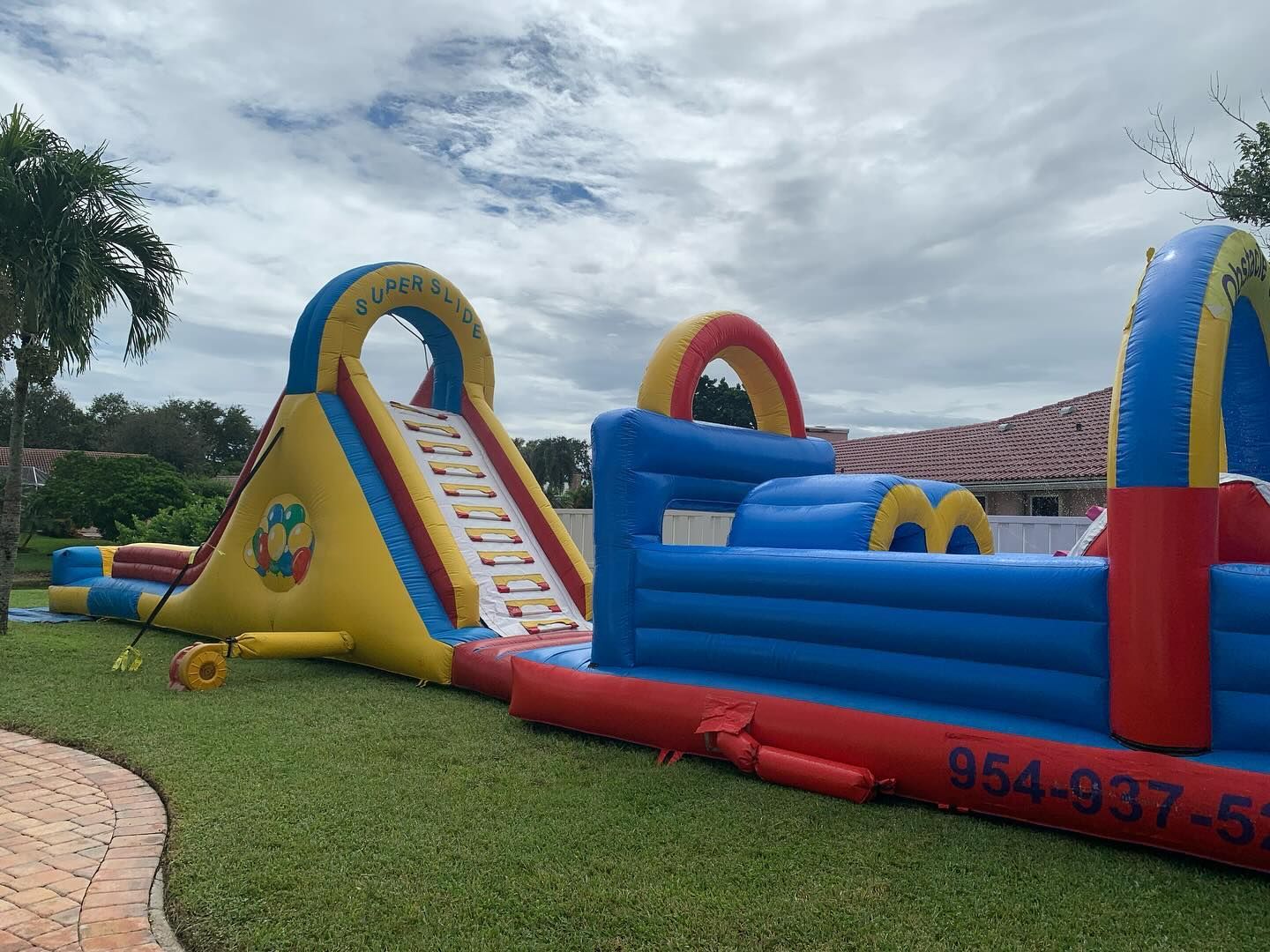 Colorful inflatable slide and obstacle course on a grassy lawn under cloudy skies
