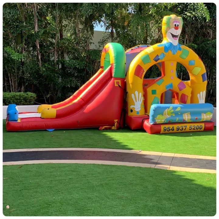 Colorful clown-themed inflatable bounce house with red slide on a grassy lawn outdoors