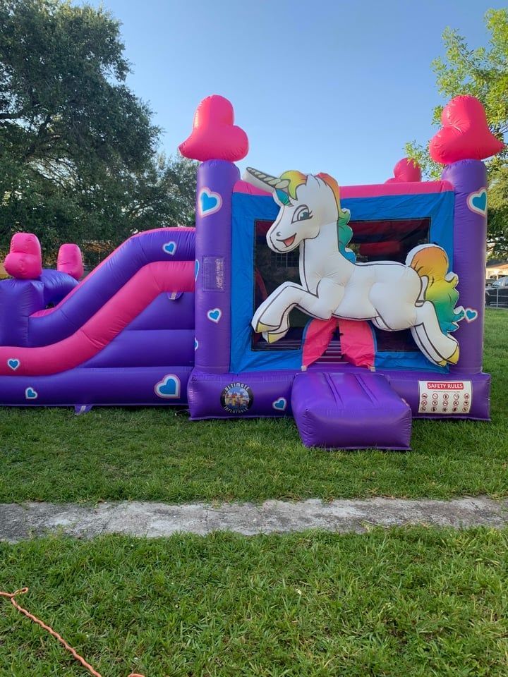 Colorful unicorn inflatable bounce house with slide and pink turrets on a grassy field