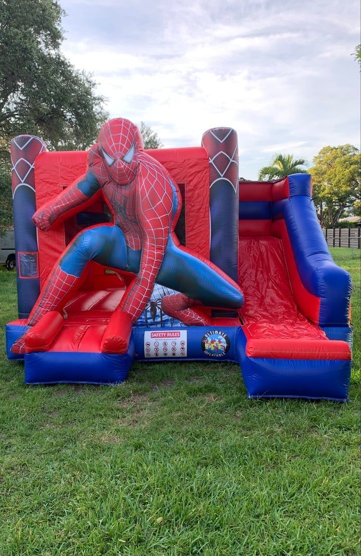 Spider-Man on a red-and-blue inflatable slide in a grassy park.