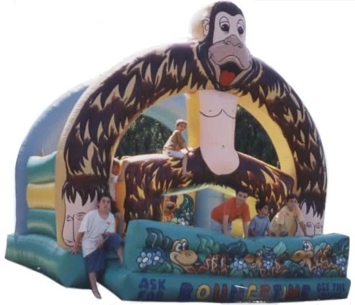 Monkey-themed inflatable bounce house with children seated at the entrance outdoors
