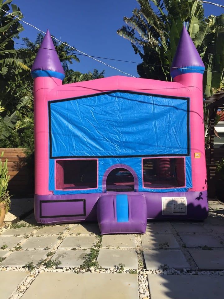 Pink-and-purple inflatable bounce house with blue front panel in a sunny backyard