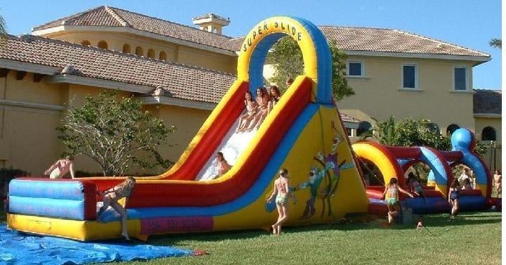 Colorful inflatable water slide with children in a backyard beside a house