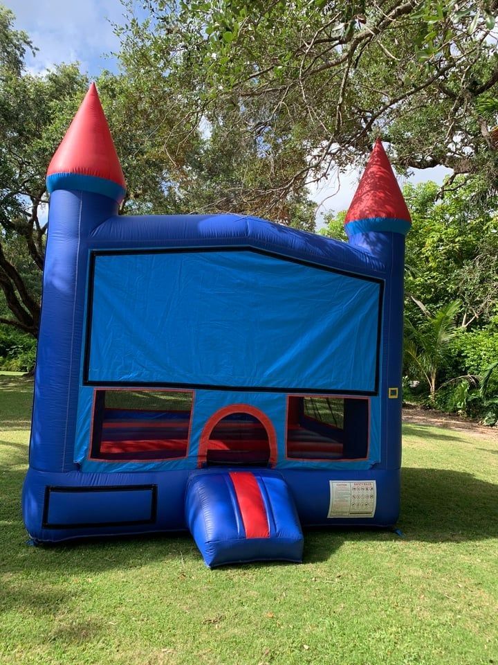 Blue castle-style bounce house with red towers and a slide in a grassy yard