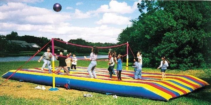 Children playing volleyball on a colorful inflatable court in a grassy park under a blue sky