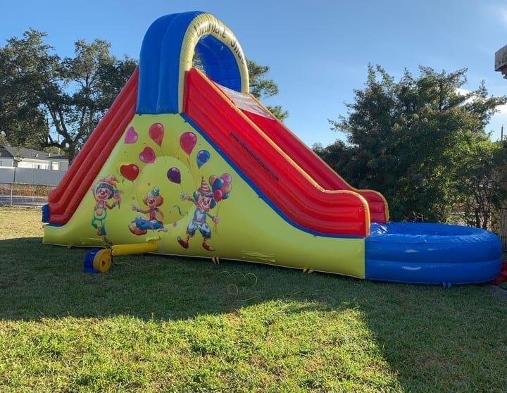 Colorful inflatable bounce slide on a grassy lawn, with red sides, blue top, and cartoon graphics.