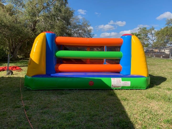 Colorful inflatable bounce house on a grassy lawn under trees, with orange, green, and blue walls.