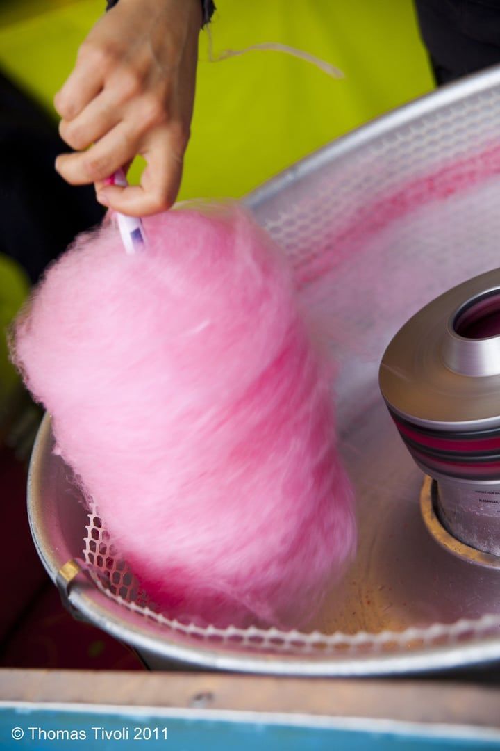 Hand pulling pink cotton candy from a machine at a fair booth