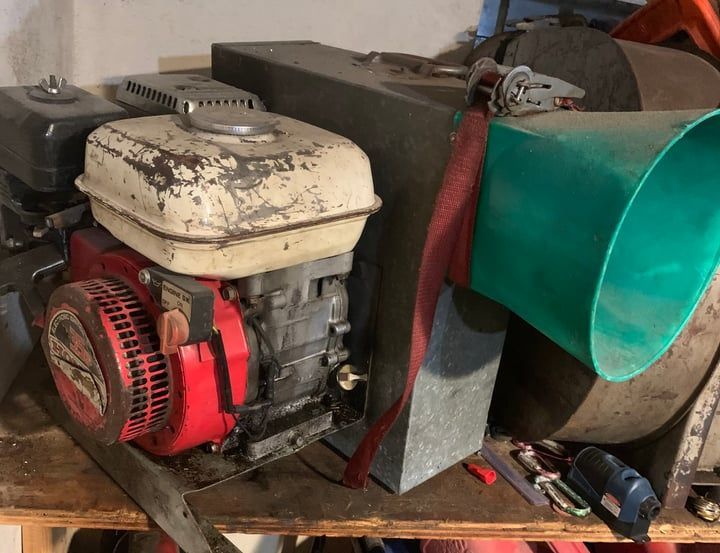 Small red-and-white engine beside a green hopper on a wooden workbench in a workshop