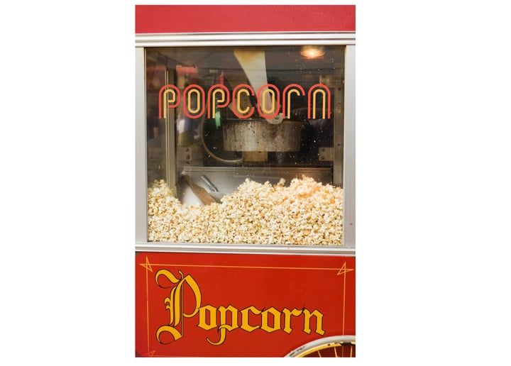 Red popcorn machine with lit sign and fresh popcorn inside a red casing