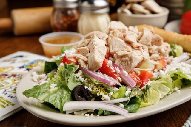 A salad with chicken , lettuce , tomatoes , onions and feta cheese on a plate on a table.