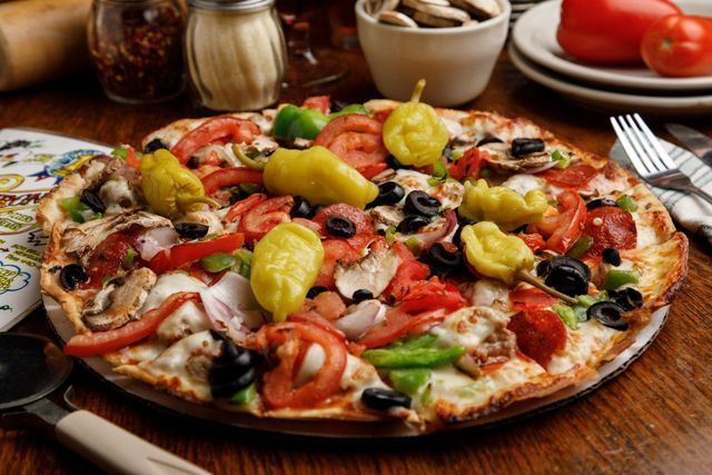 A pizza with a lot of vegetables on it is on a wooden table.