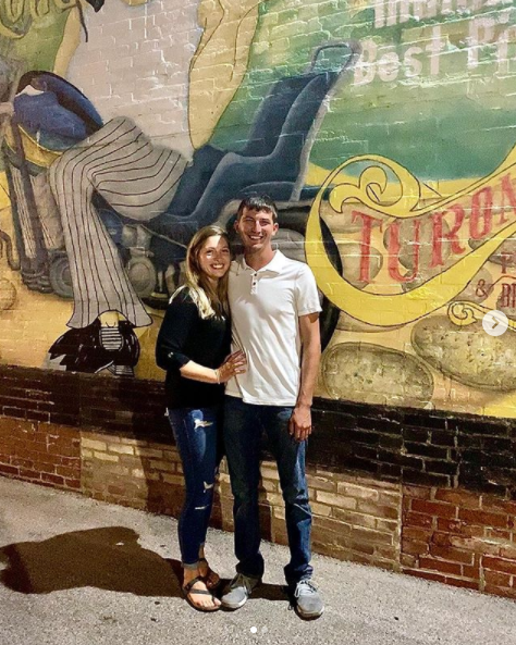 A man and a woman are standing in front of a mural on a brick wall.