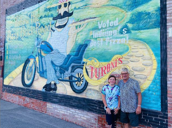 A man and woman are standing in front of a mural of a man riding a motorcycle.