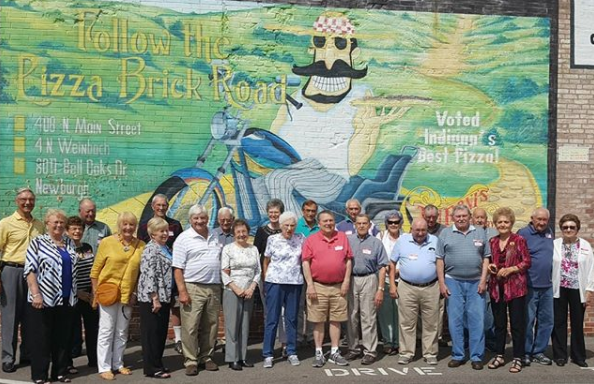 A group of people are posing for a picture in front of a mural of a man on a motorcycle.