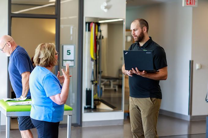 A man is holding a laptop and talking to a woman in a hospital.