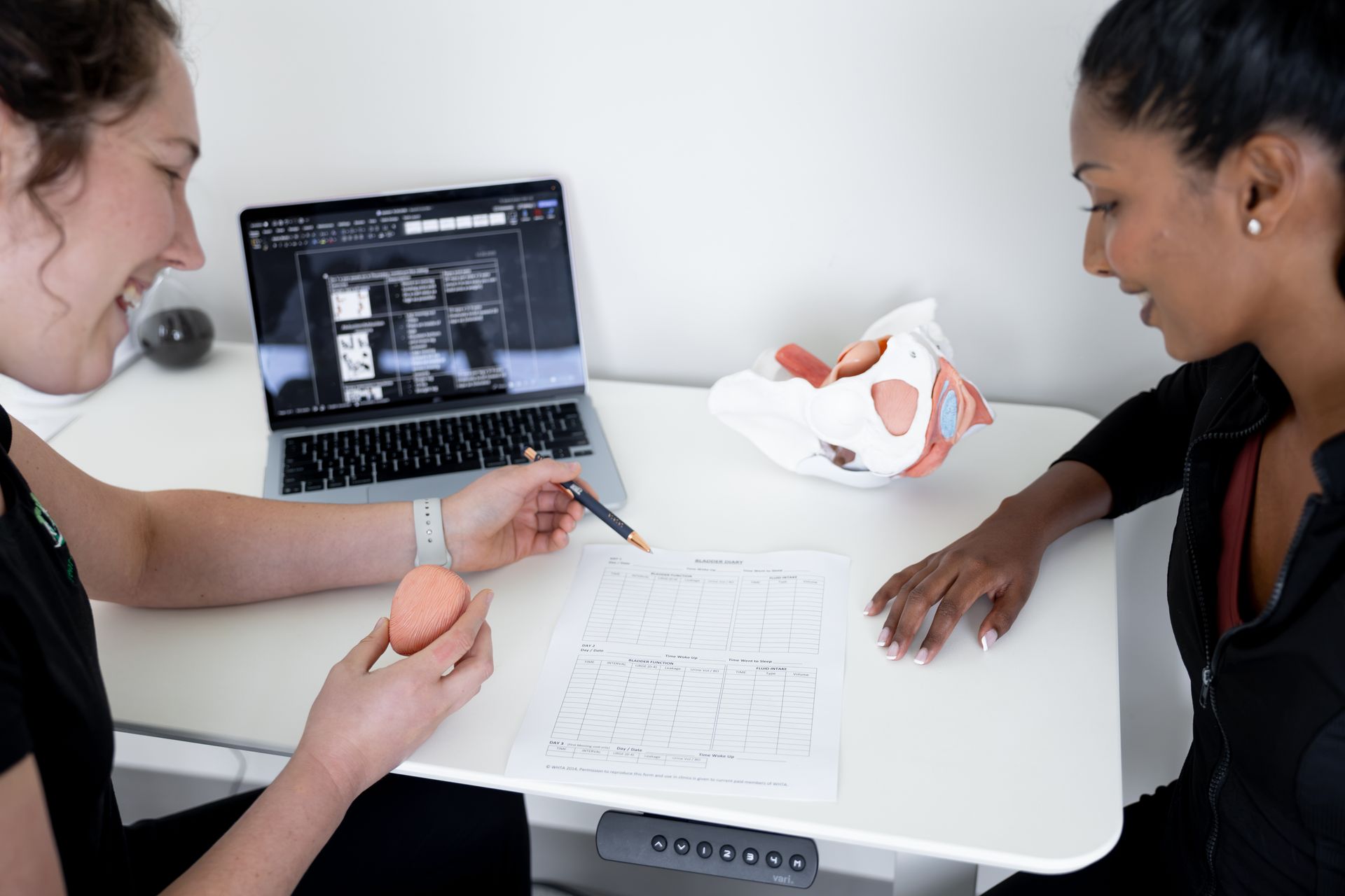 Two people reviewing sketches at a white table with a laptop and sample object in a bright office