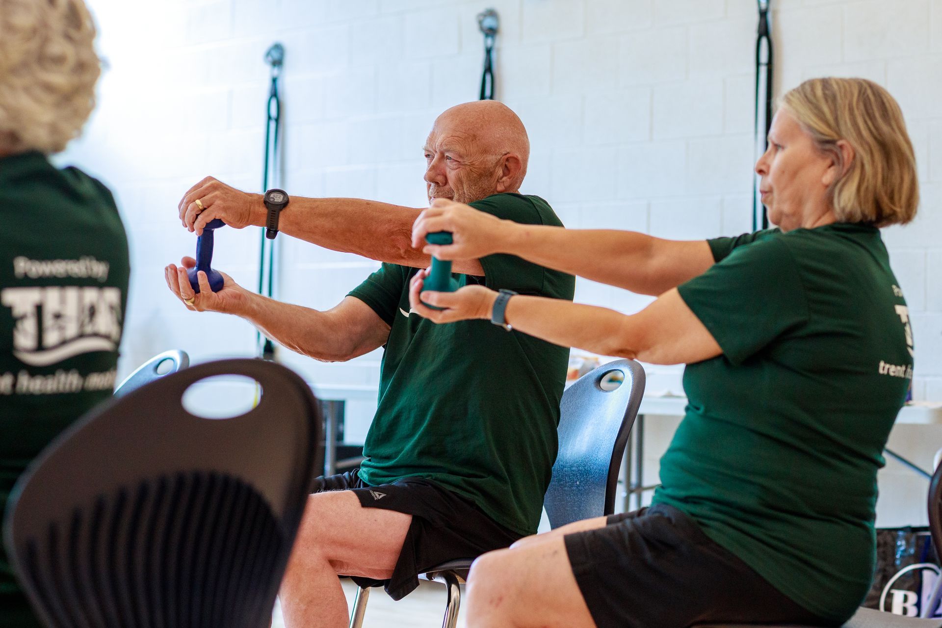 A woman in a green shirt is holding dumbbells in a gym
