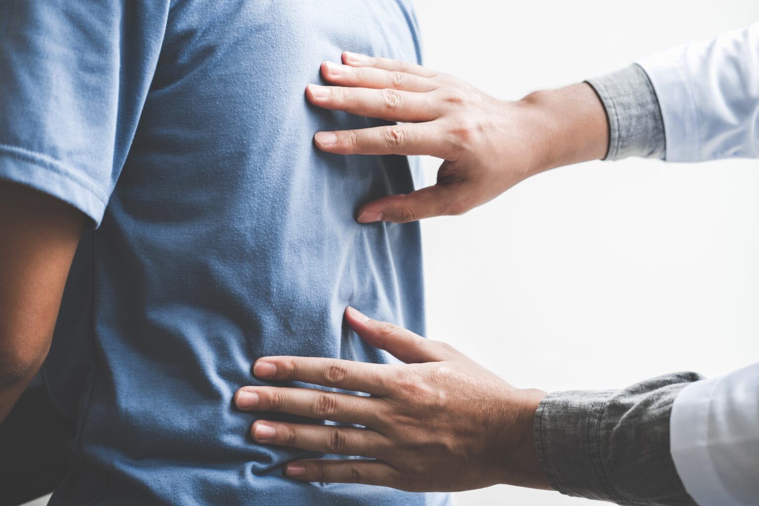 Doctor examining a patient's back. Hands on back, white coat sleeves, blue shirt.