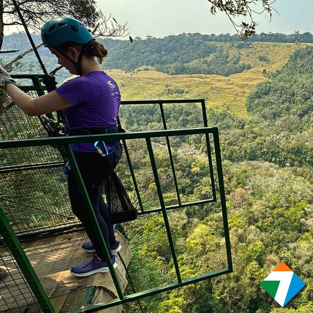 Mulher com equipamento de segurança em plataforma com vista para um vale exuberante.